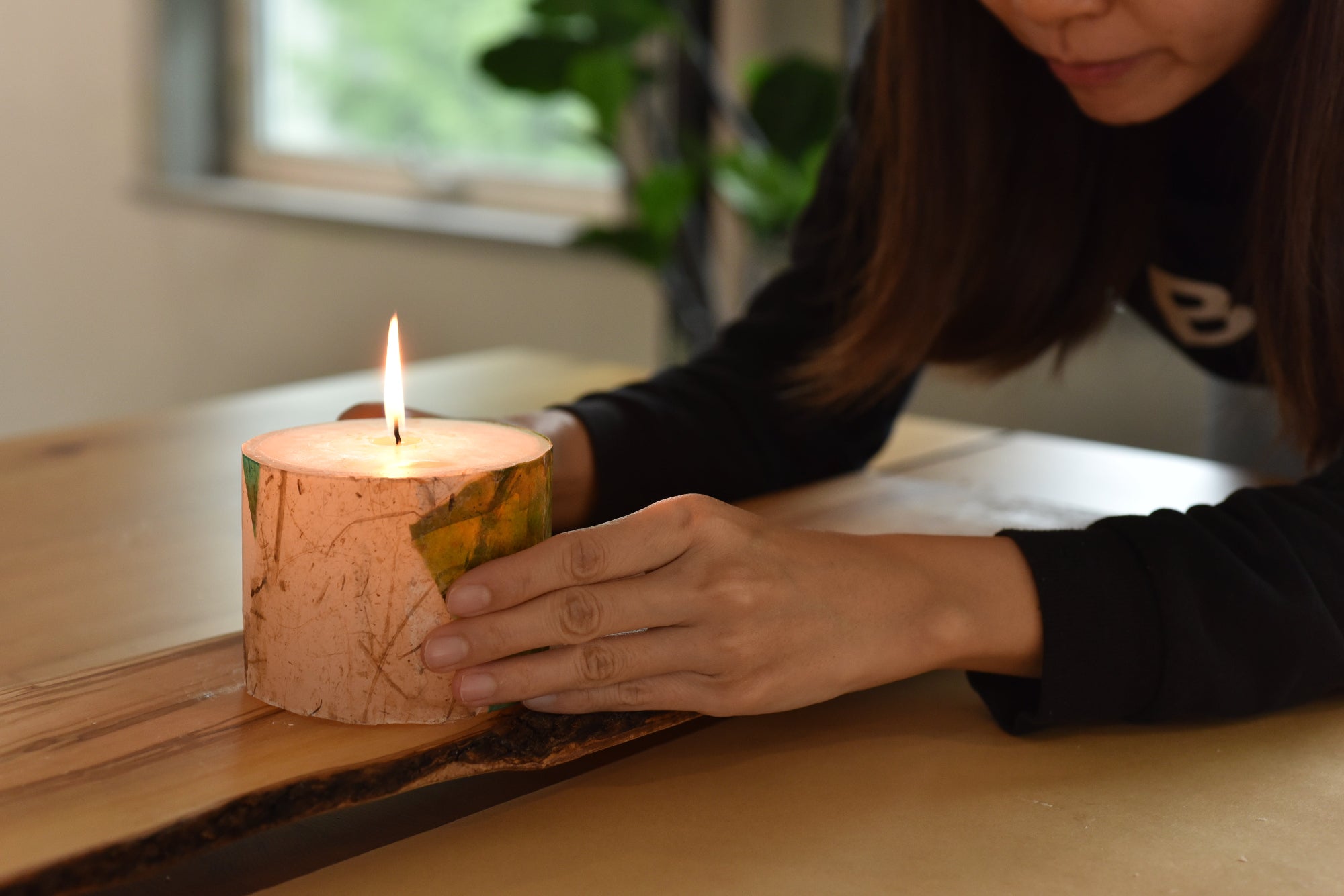 Person holding a lit candle with a wooden base on a table